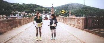 Zwei Tänzerinnen schauen sich an. Sie stehen auf der Alten Brücke Heidelberg.